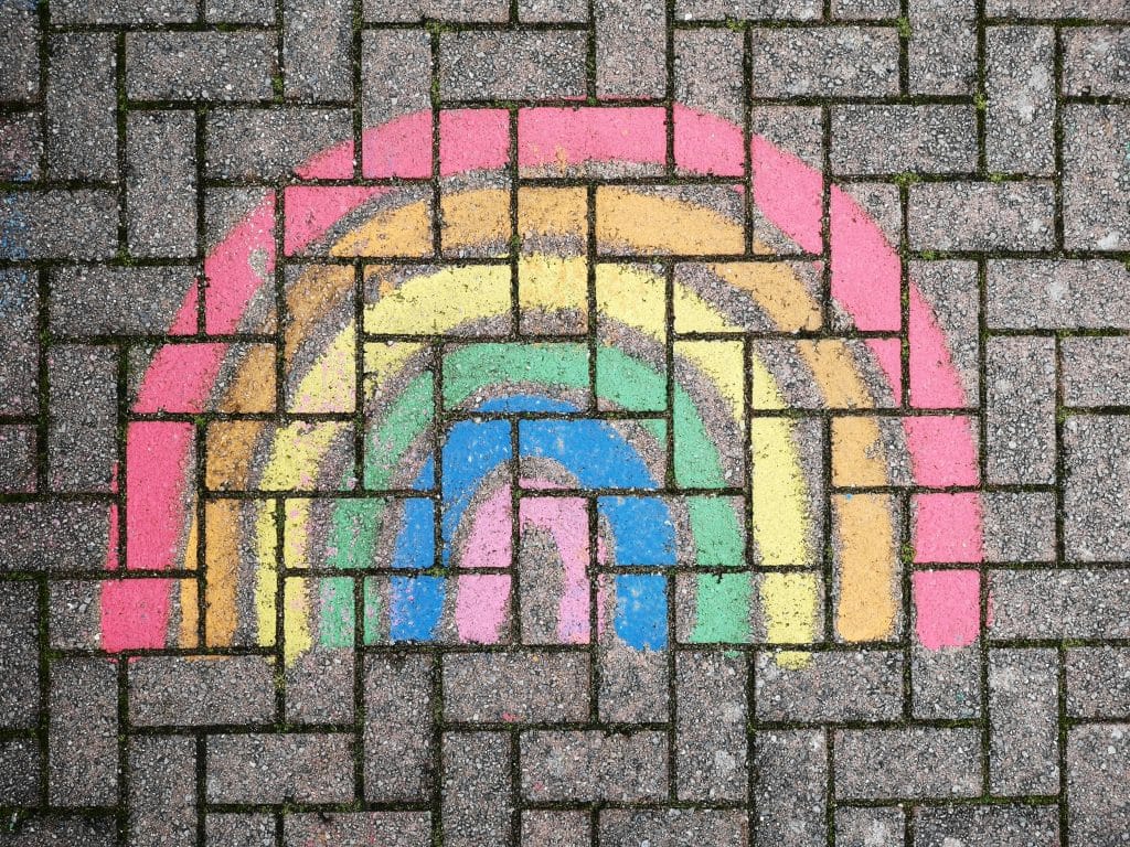 A vibrant rainbow drawn with chalk on a textured brick pavement, adding color to an urban setting.